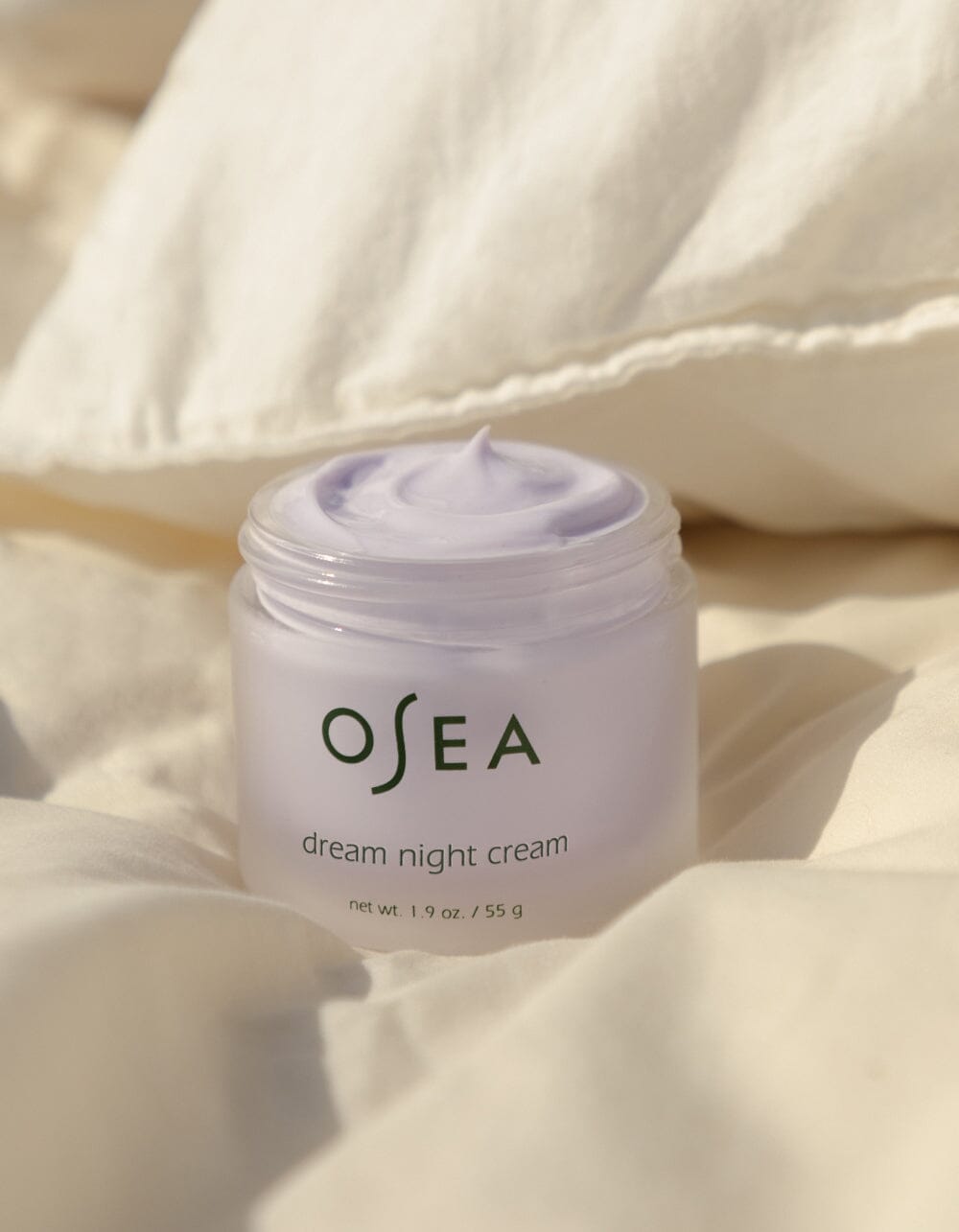 OSEA Dream Night Cream opened and placed on soft cream-colored bedding