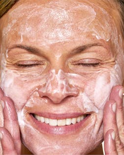 Close-up of a woman applying a cleansing milk  to her face.