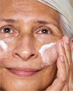 Mature model applying cream from Ritual Reset Bundle with glowing skin
