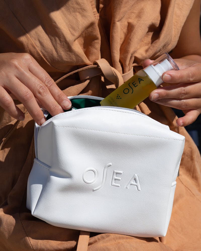 Person holding a white pouch with 'OSEA' branding, next to a bottle of OSEA product.