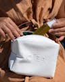 Person placing OSEA skincare bottle into white zippered cosmetic bag for travel