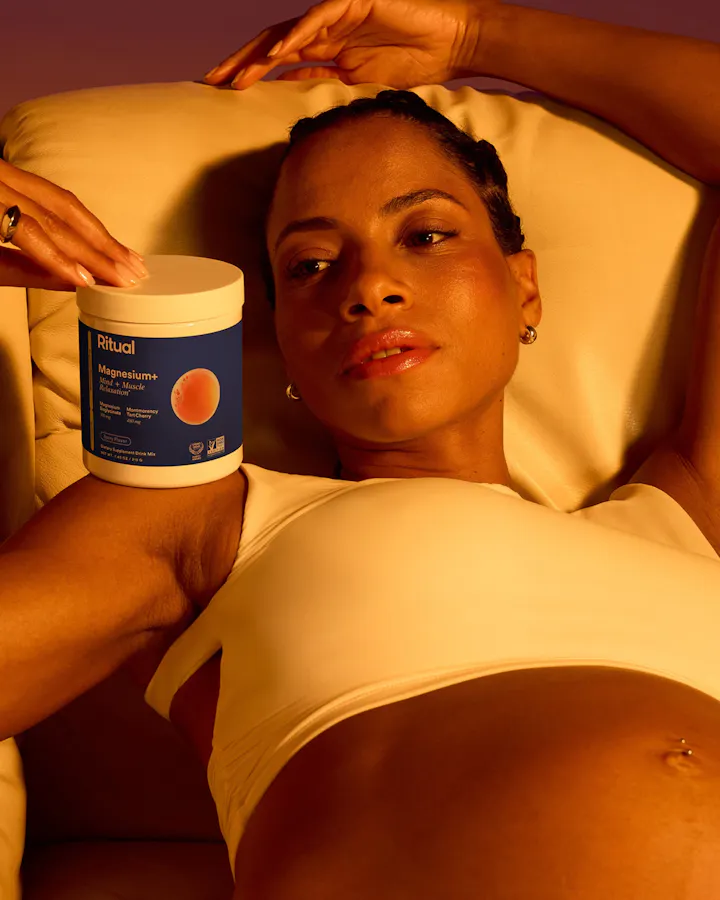 Model reclining while holding Ritual Magnesium+ Mind & Muscle Relaxation supplement