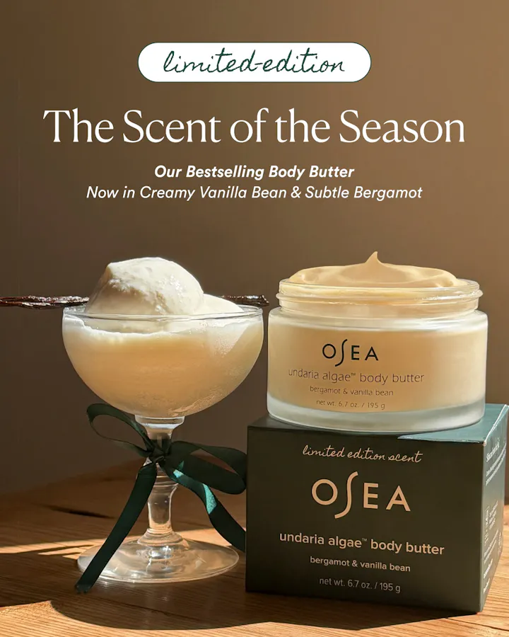 Open jar of OSEA Undaria Algae Body Butter in Bergamot & Vanilla Bean atop its limited edition packaging box, styled outdoors against a blue sky and ocean horizon with a ribboned gift box beside it.