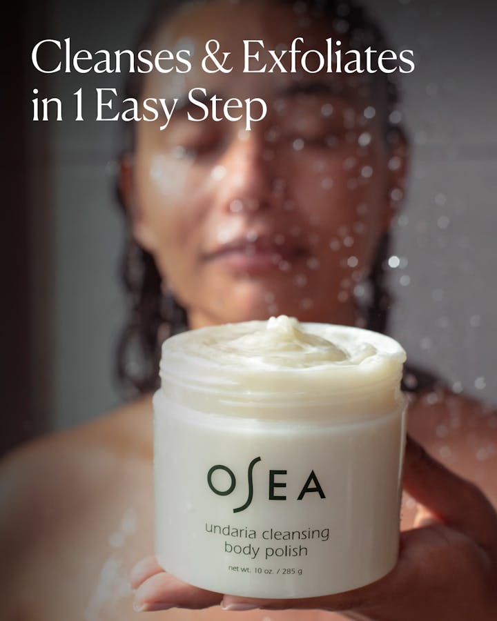 OSEA body polish jar held by a person with showerhead in background