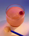 Glass of pink Ritual drink with branded ice cube, cherry garnish, and powder scoop on gradient background