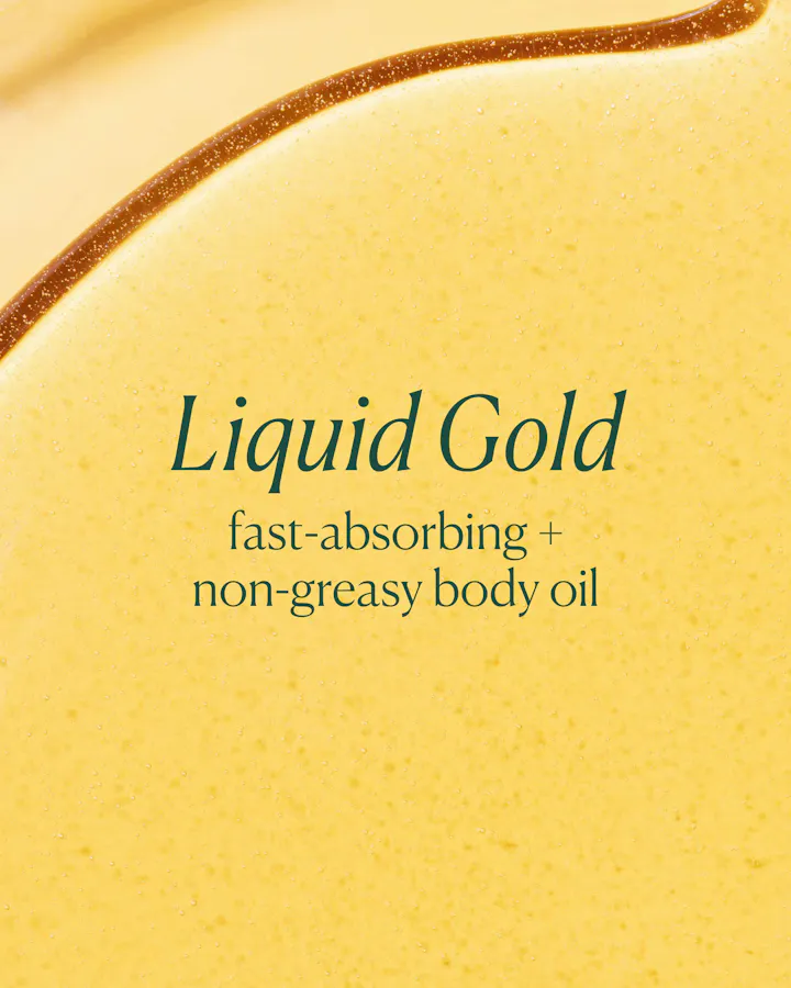 Close-up of a yellow body oil with 'Liquid Gold' text on a beige background