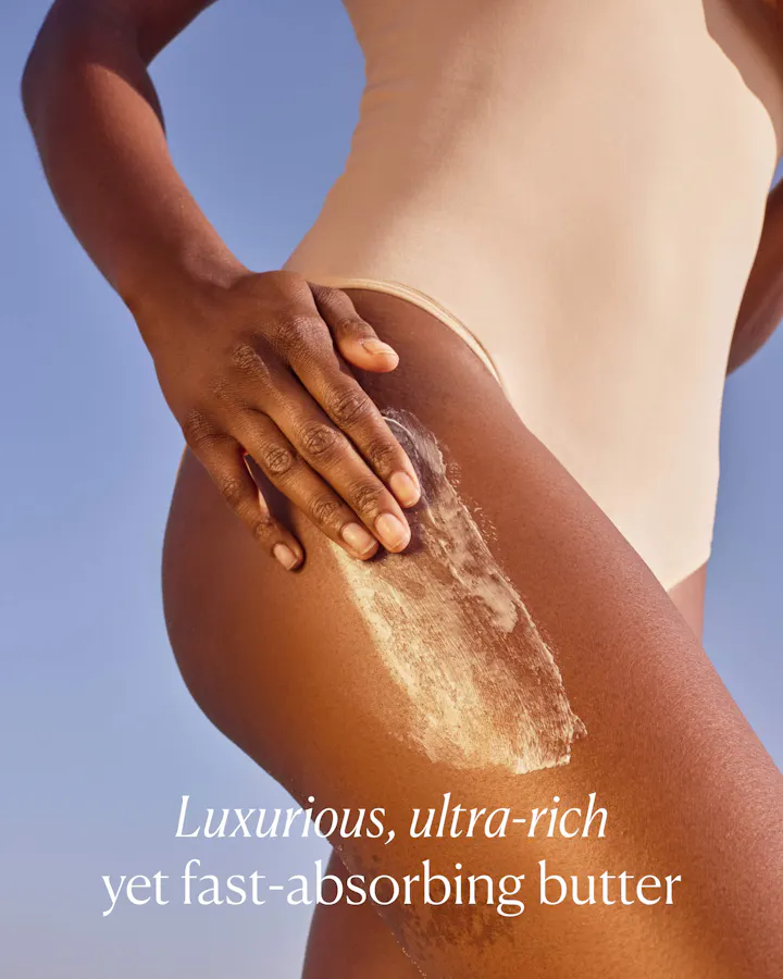 Person applying luxurious ultra-rich butter to their skin with a clear blue sky background