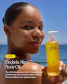 A woman outdoors by the ocean holds a yellow OSEA Undaria Algae Body Oil bottle. The image includes promotional text on the left side.