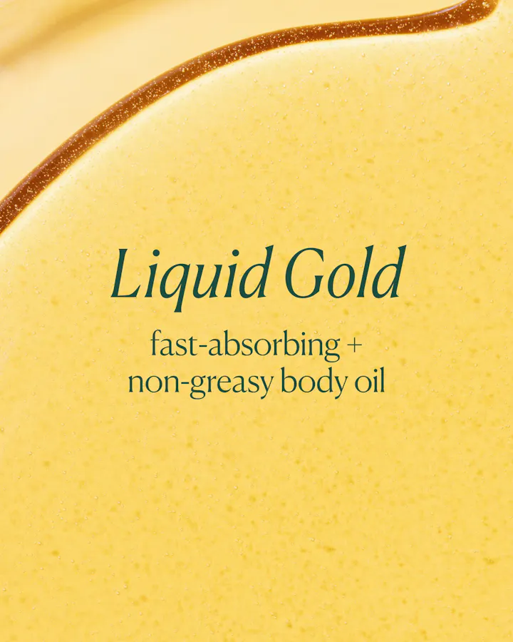 A close-up of a golden yellow liquid body oil with the text 'Liquid Gold' and 'fast-absorbing + non-greasy body oil' printed in dark green on the surface.