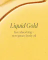 A close-up of a golden yellow liquid body oil with the text 'Liquid Gold' and 'fast-absorbing + non-greasy body oil' printed in dark green on the surface.