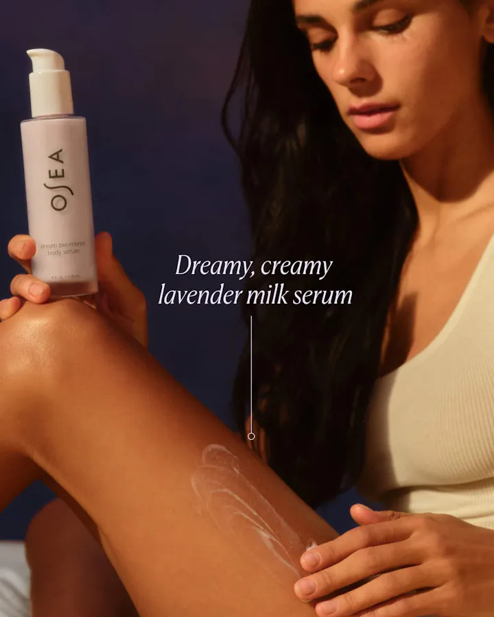 Woman applying Ojea lavender milk serum to her arm with a dark background