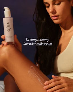 Woman applying OSEA lavender milk serum to her arm with a dark background
