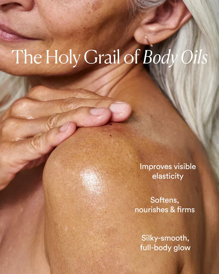 Close-up of a hand applying oil to a shoulder, with text reading 'The Holy Grail of Body Oils: Improves visible elasticity, softens, nourishes & firms, silky-smooth full-body glow.'