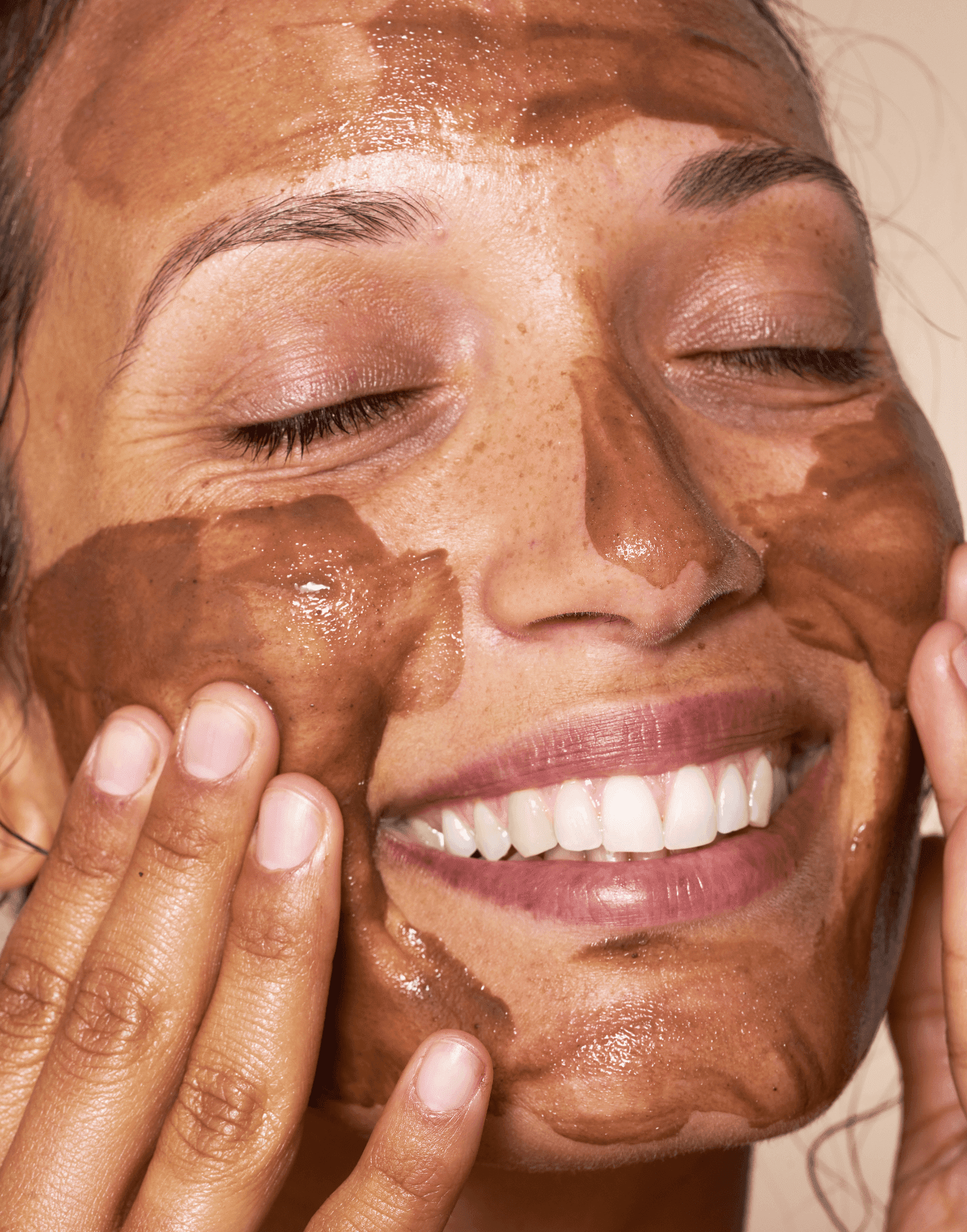 Model smiling while applying OSEA Ocean Cleansing Mudd mask to face