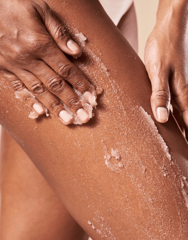 Person scrubbing their leg with a exfoliating product