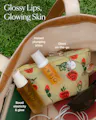 Osea skincare products arranged inside a beige tote bag on green grass, including a strawberry-print pouch and two amber bottles with white caps. White text overlays describe the products and benefits.
