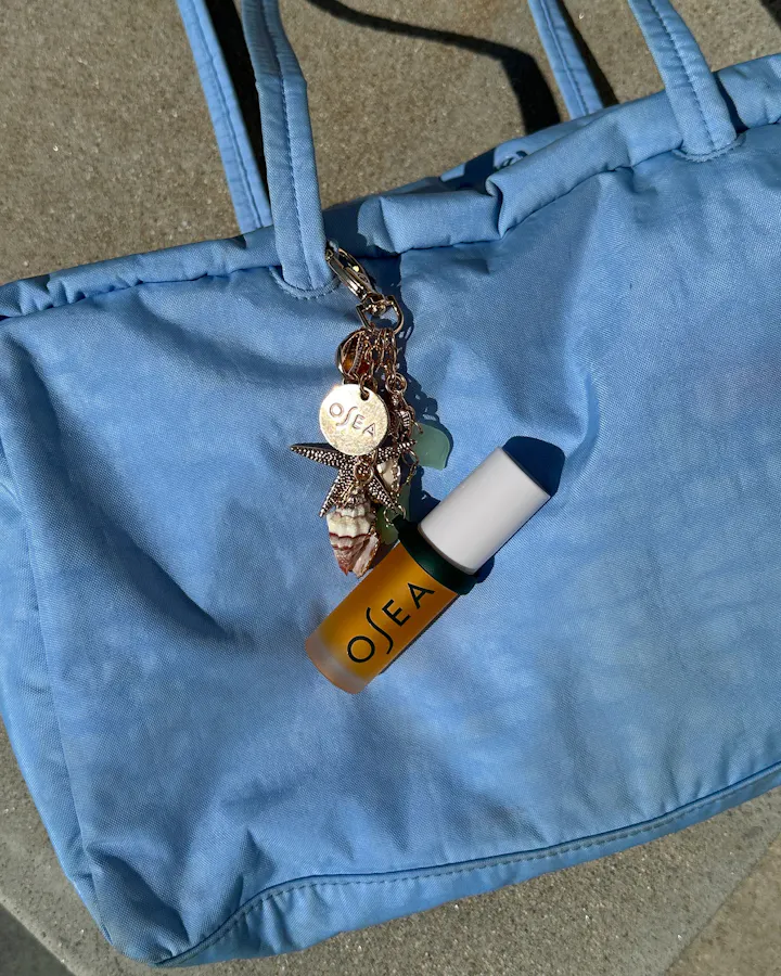 OSEA lip oil keychain clipped onto light blue tote bag