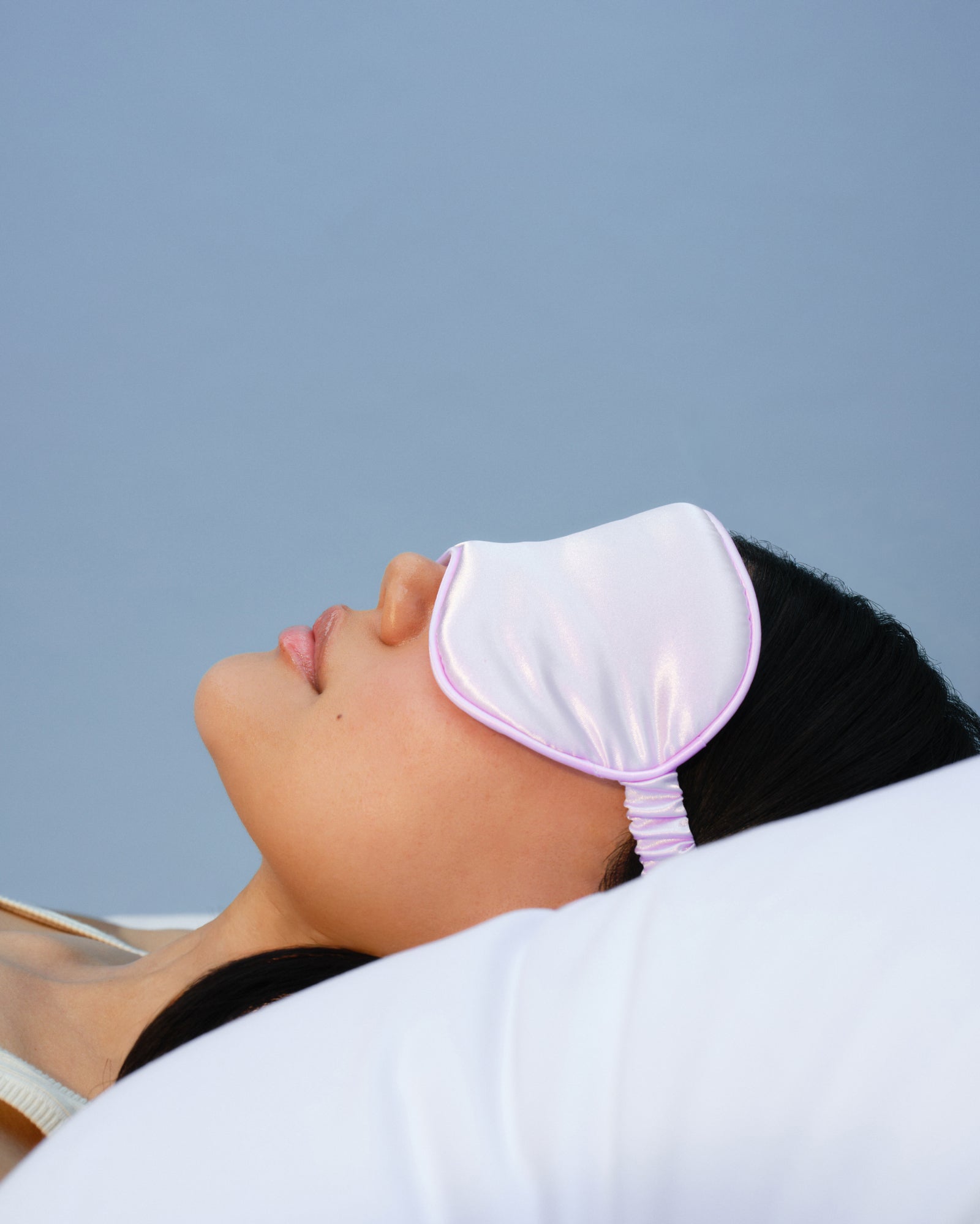 Person wearing a white sleep mask against a light blue background