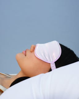 Person wearing a white sleep mask against a light blue background