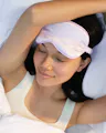 Woman relaxing in bed wearing OSEA lavender satin sleep mask for a calming nighttime ritual