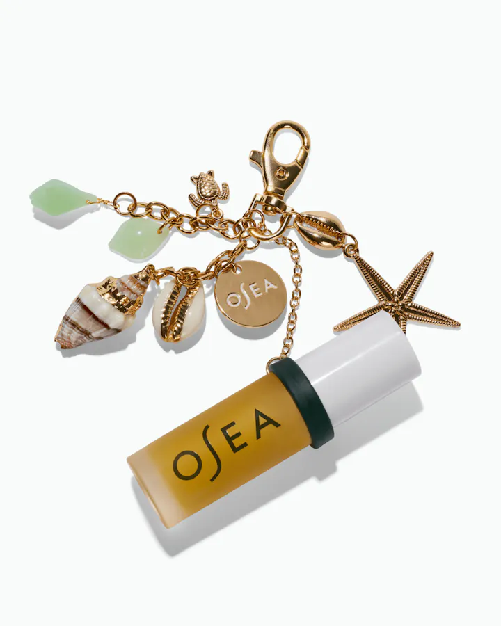 OSEA lip oil attached to gold ocean-inspired charm keychain on white background