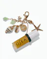 OSEA lip oil attached to gold ocean-inspired charm keychain on white background