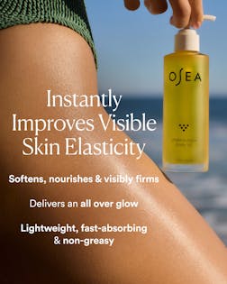 OSEA body oil bottle with text about skin elasticity improvement against a blurred beach background