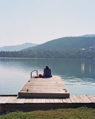 A Woman Sits On A Dock Overlooking A Lake