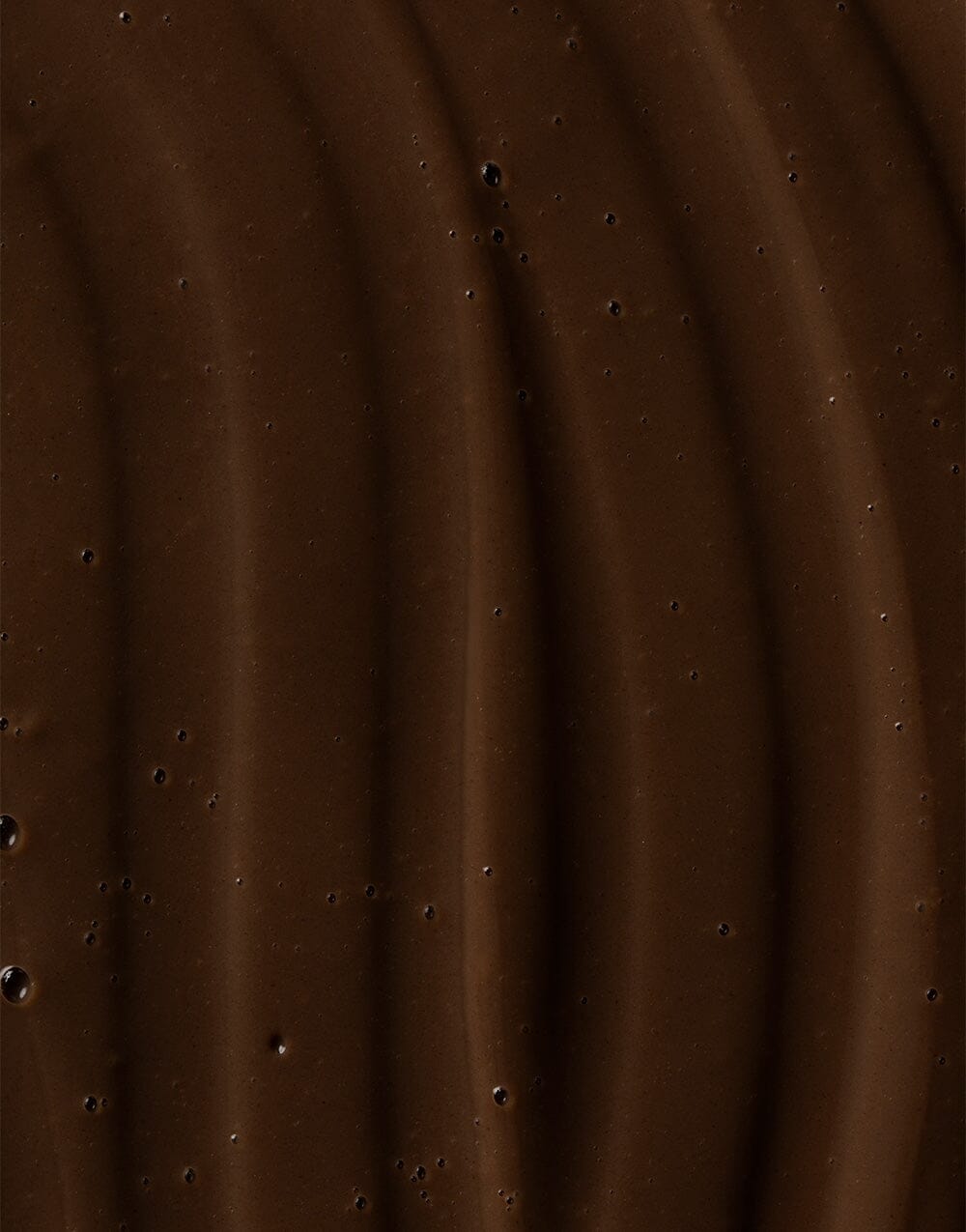 Close-up of rich, dark brown Ocean Cleansing Mudd texture with wavy surface pattern