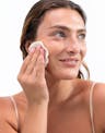 Model gently using a reusable OSEA cleansing pad to remove makeup from her cheek