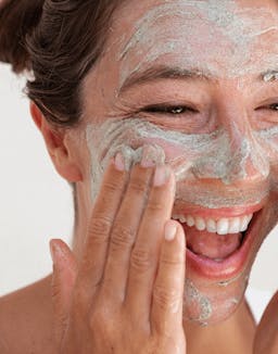 Model smiling while applying OSEA Seaglow Scrub to face with visible texture