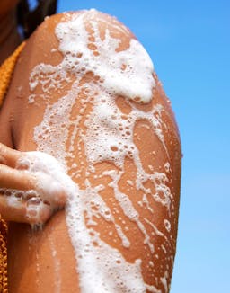 Model lathering OSEA cleanser or body wash on leg under bright blue sky

