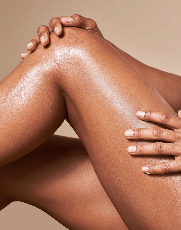 Model applying OSEA Anti-Aging Body Balm to legs, highlighting glowing skin