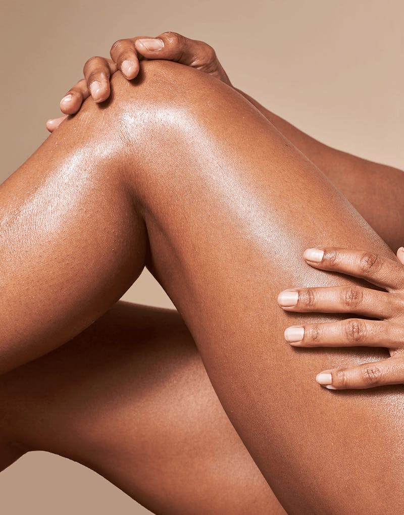 Model applying OSEA Anti-Aging Body Balm to legs, highlighting glowing skin