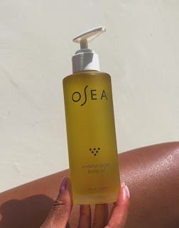 Hand holding OSEA Undaria Algae Body Oil bottle upright in natural light