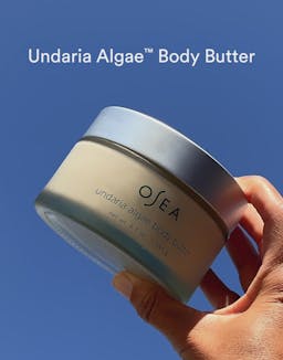 Hand holding OSEA Undaria Algae Body Butter against a blue sky background