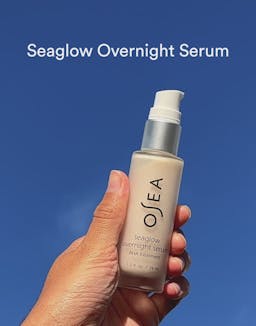 Hand holding OSEA Seaglow Overnight Serum upright in natural light
