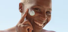 Woman Smiling While Applying A Cream To Her Face