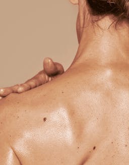 Model using OSEA body brush on upper back in soft natural lighting