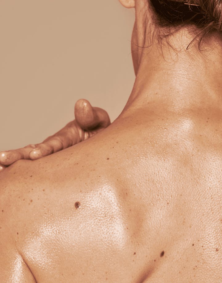 Model using OSEA body brush on upper back in soft natural lighting