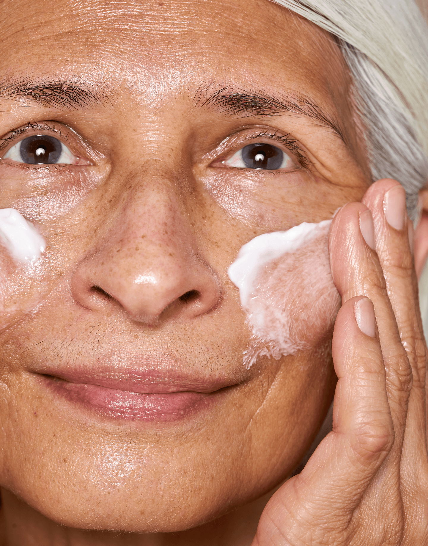 Mature model applying Advanced Protection Cream to cheek in natural lighting