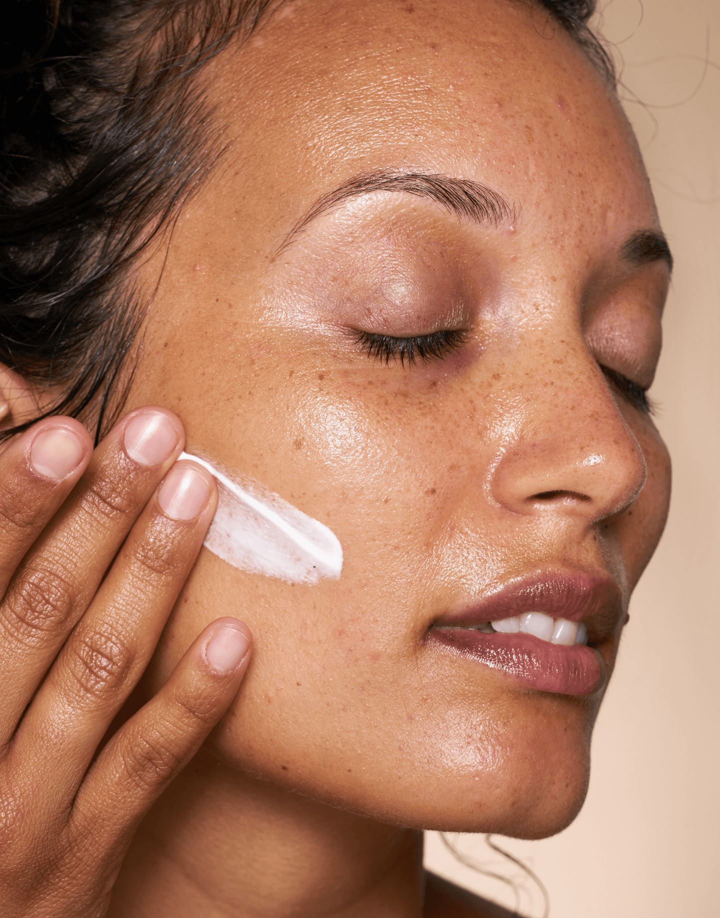 Model applying OSEA Atmosphere Protection Cream to cheek with gentle smile