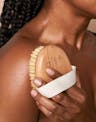 Model using OSEA dry body brush on shoulder to exfoliate and stimulate skin