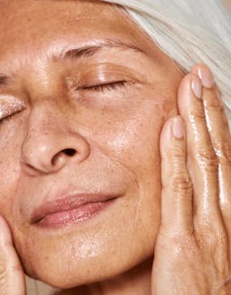 Mature model applying oil with serene expression, highlighting glow