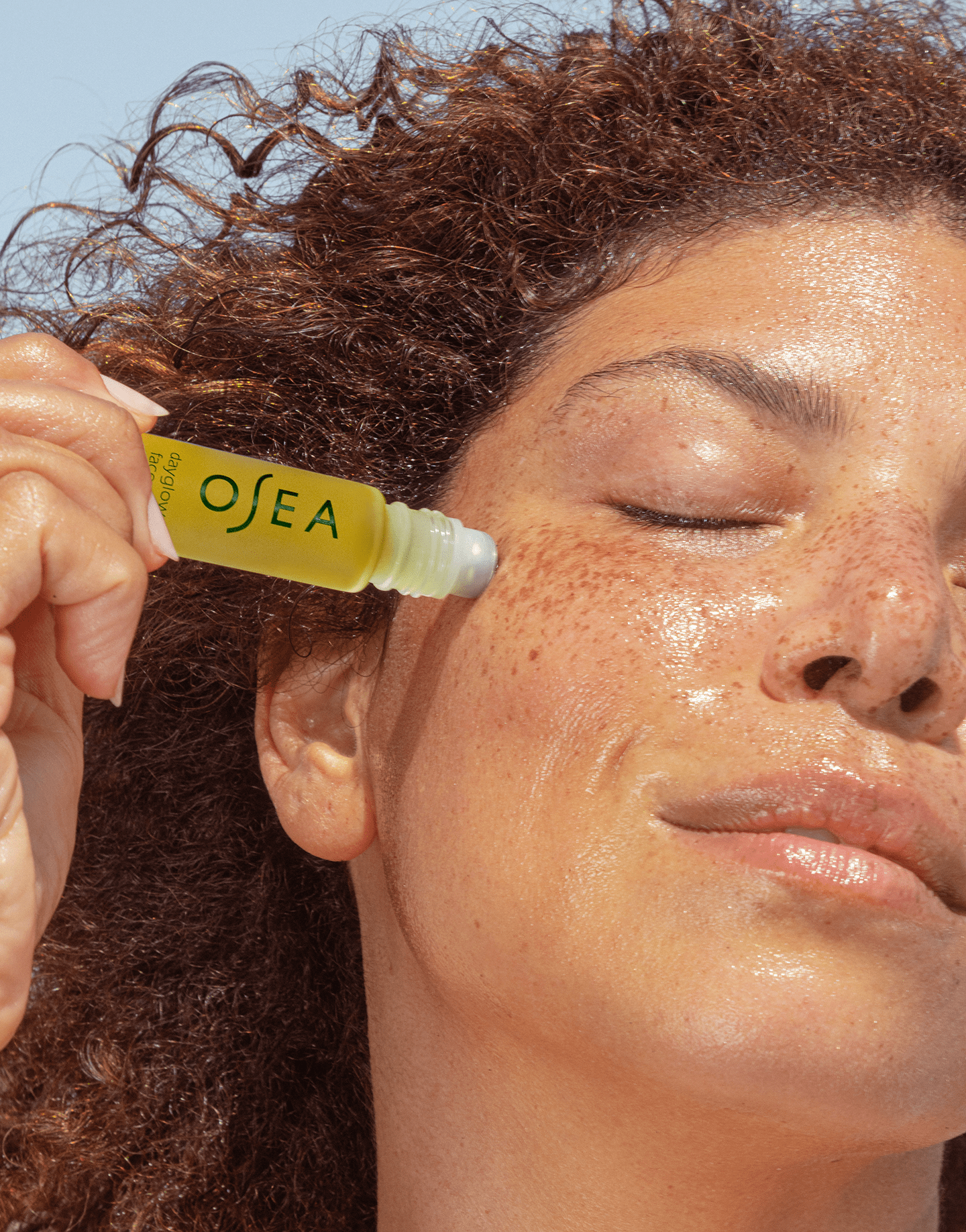 Model smiling and applying OSEA product dropper to cheek in bright natural light