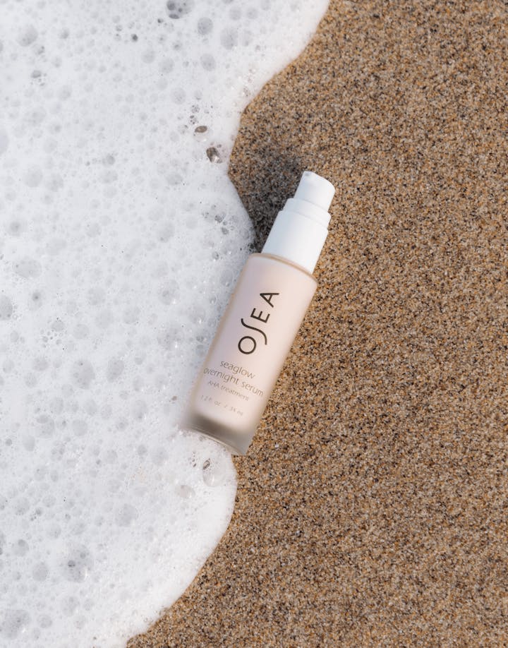 Seaglow Overnight Serum bottle resting on soft sand near shoreline